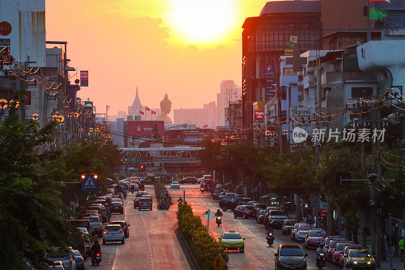 橙色的夕阳天空在佛祖Dhammakaya Thep Mongkol(青铜雕像)和Wat Paknam Bhasicharoen(皇家寺庙)之上，从立交桥上看高速公路上的交通堵塞，摩托车，汽车，空气污染，烟雾，汽车烟雾，重点在前景